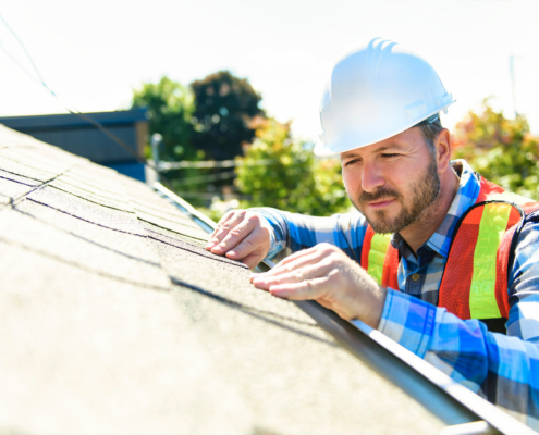 man with hard hat standing on steps inspecting house roof