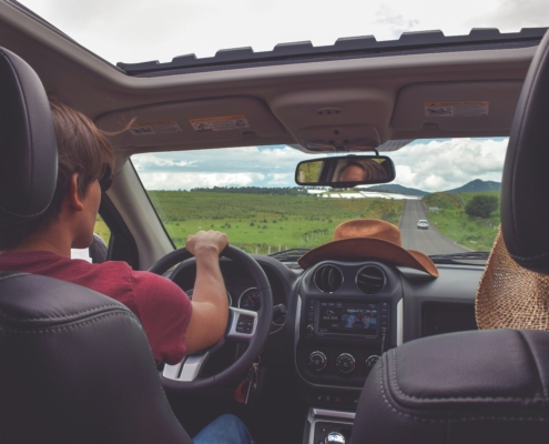 A first-person perspective of a summer road trip, featuring a driver behind the wheel, a sunny open road ahead, and a wide-open sunroof reflecting an adventurous atmosphere.