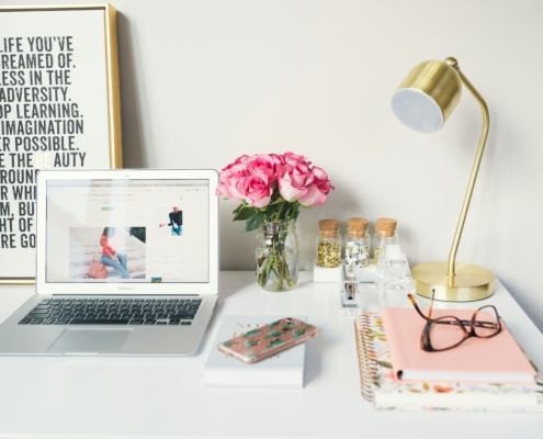 A bright and stylish workspace with gold accents, floral decor, and a silver laptop, creating a professional yet cozy "work from home" atmosphere.